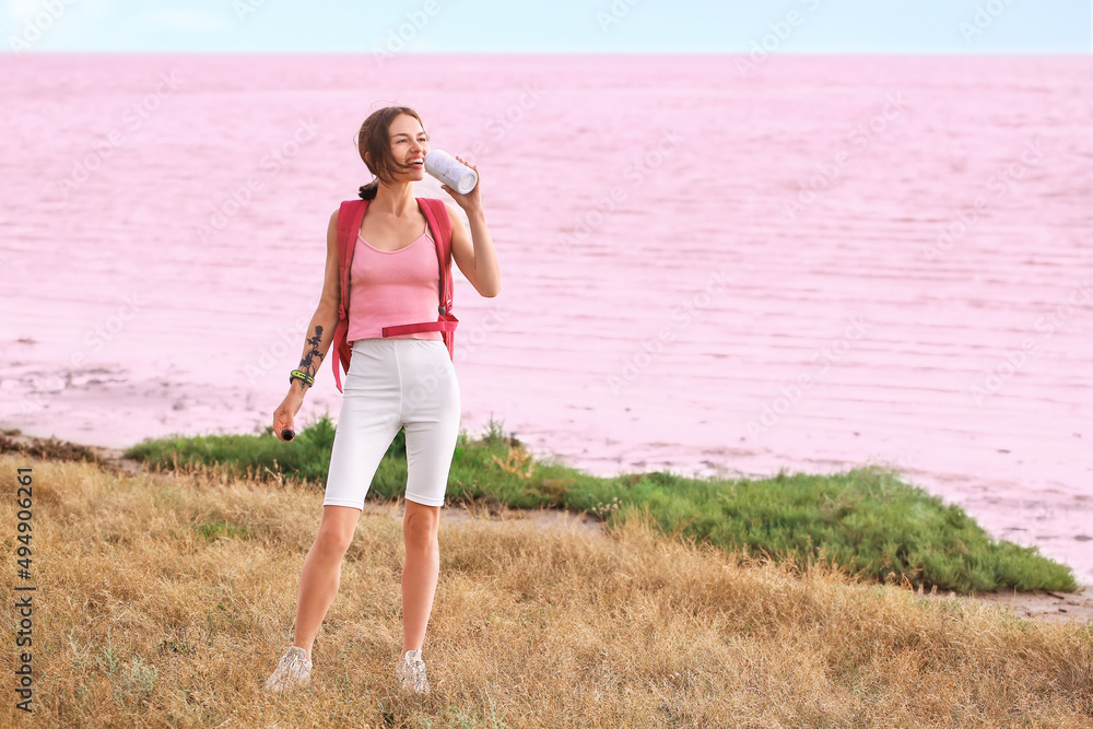 Young tourist with backpack drinking water near pink lake