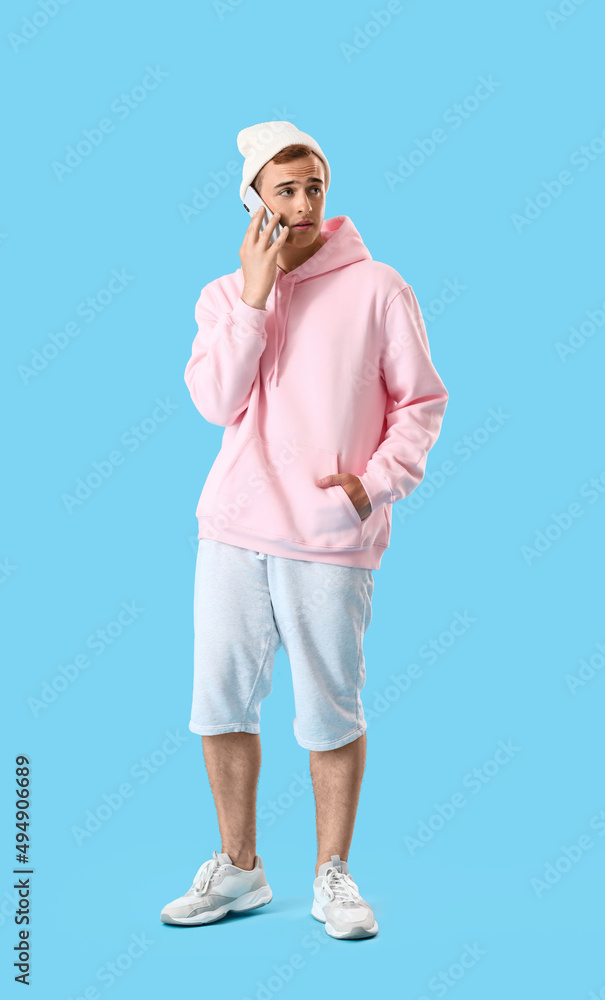 Young guy in stylish hoodie talking by phone on color background