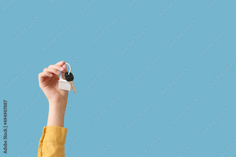 Young woman with key from house on blue background