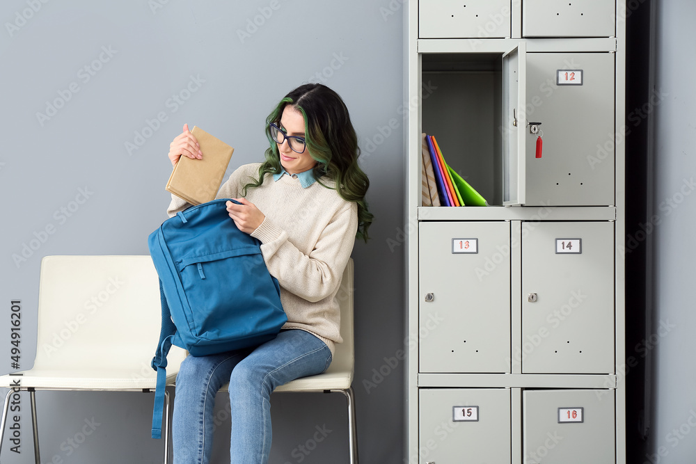 漂亮的女学生坐在大学储物柜附近，把书放在背包里