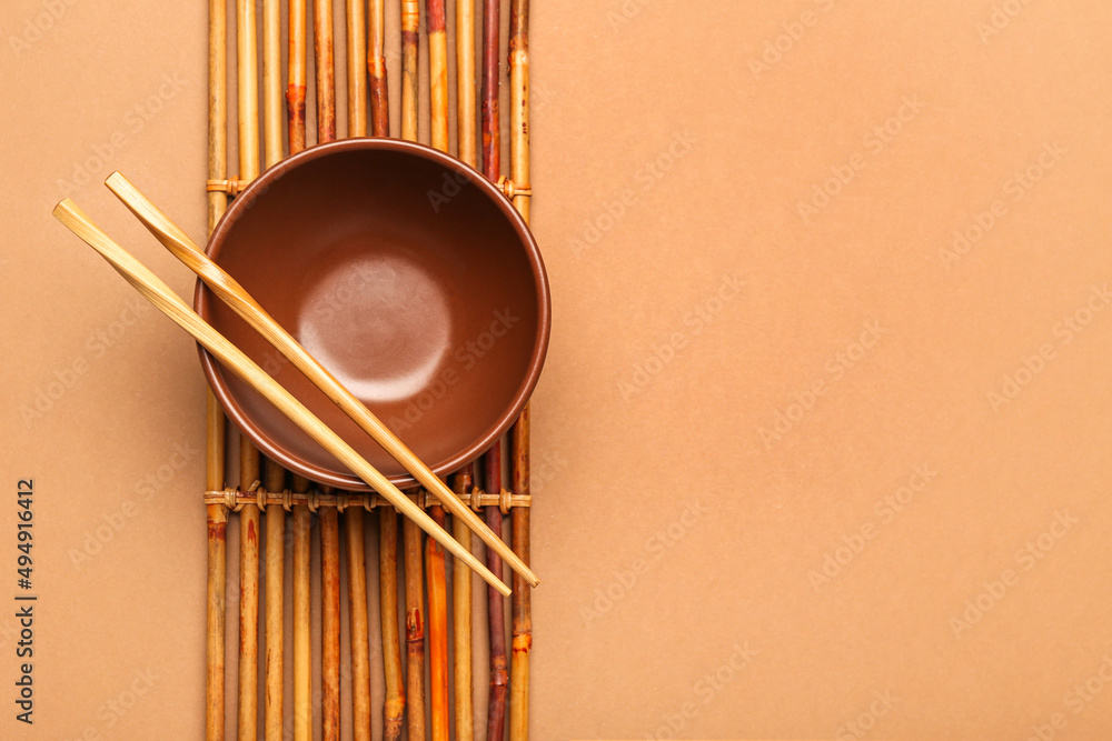 Bamboo mat with Chinese bowl and chopsticks on color background