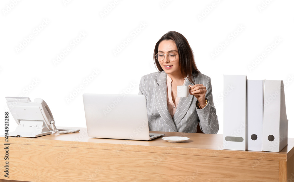 Young secretary with laptop drinking coffee at table on white background