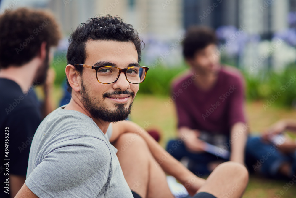 Loving life on campus. Portrait of a cheerful young man sitting in the park with his friends and stu