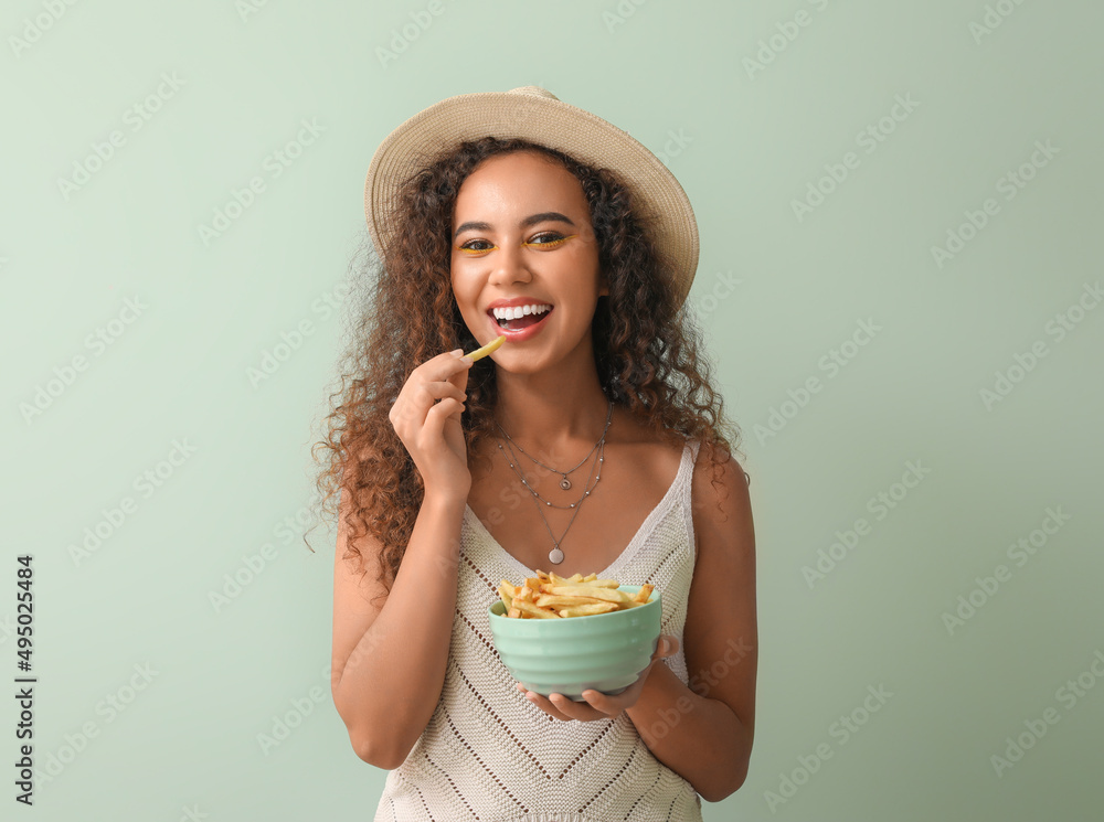 Young African-American woman with french fries on color background