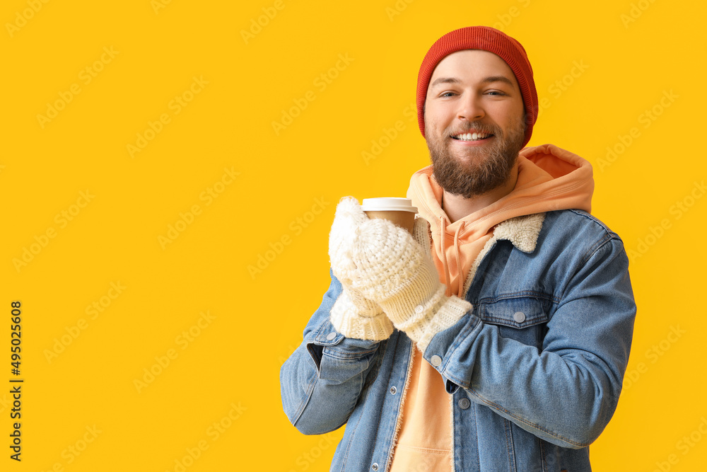 戴着温暖手套的留胡子的年轻人，黄色背景上有一杯咖啡