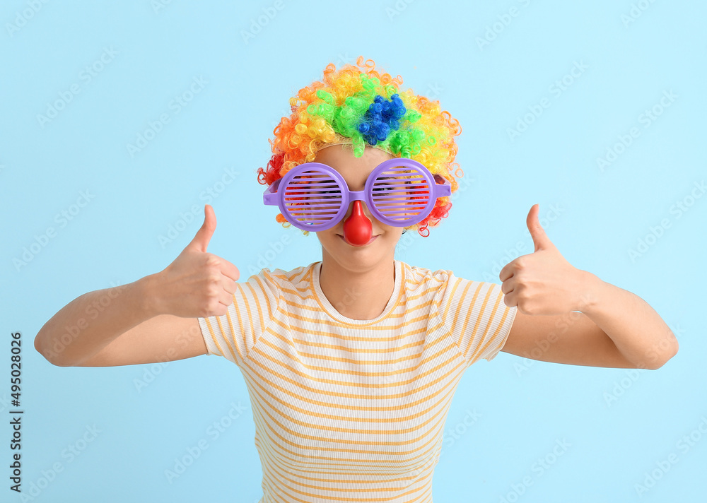 Young woman in funny disguise showing thumbs-up on blue background. April Fools Day celebration