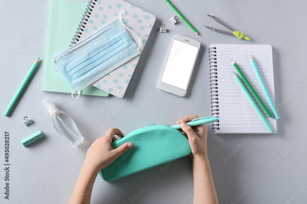 Childs hands with pencil case, medical mask, mobile phone and stationery on white background