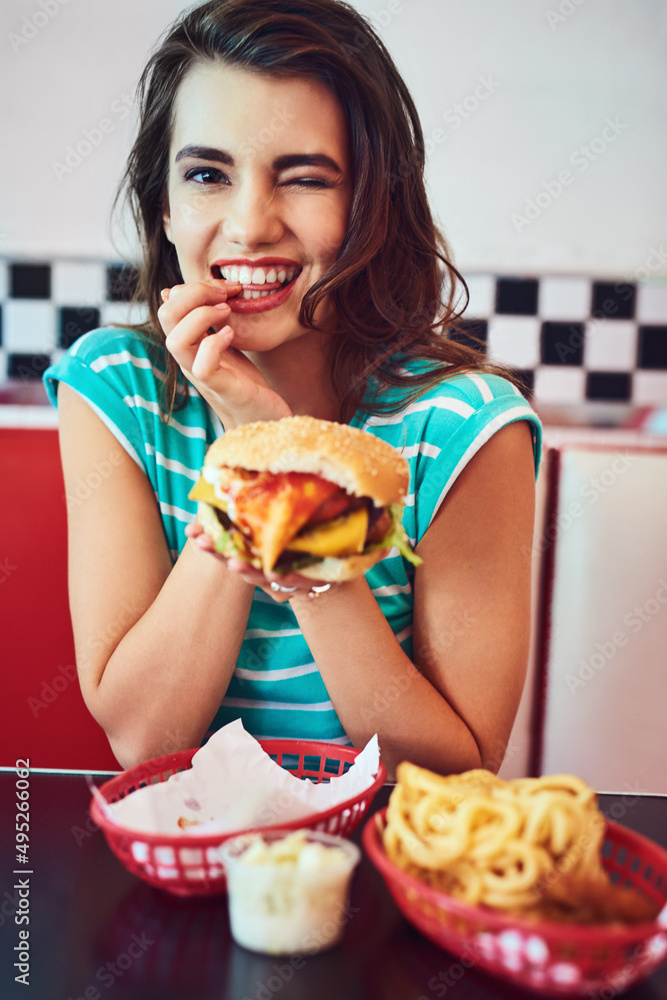 I eat very well. Cropped portrait of an attractive young woman enjoying a burger in a retro diner.