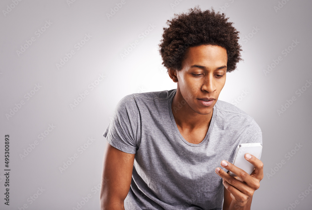 Solving lifes dilemmas one app at a time. Shot of a young man using his cellphone against a gray bac