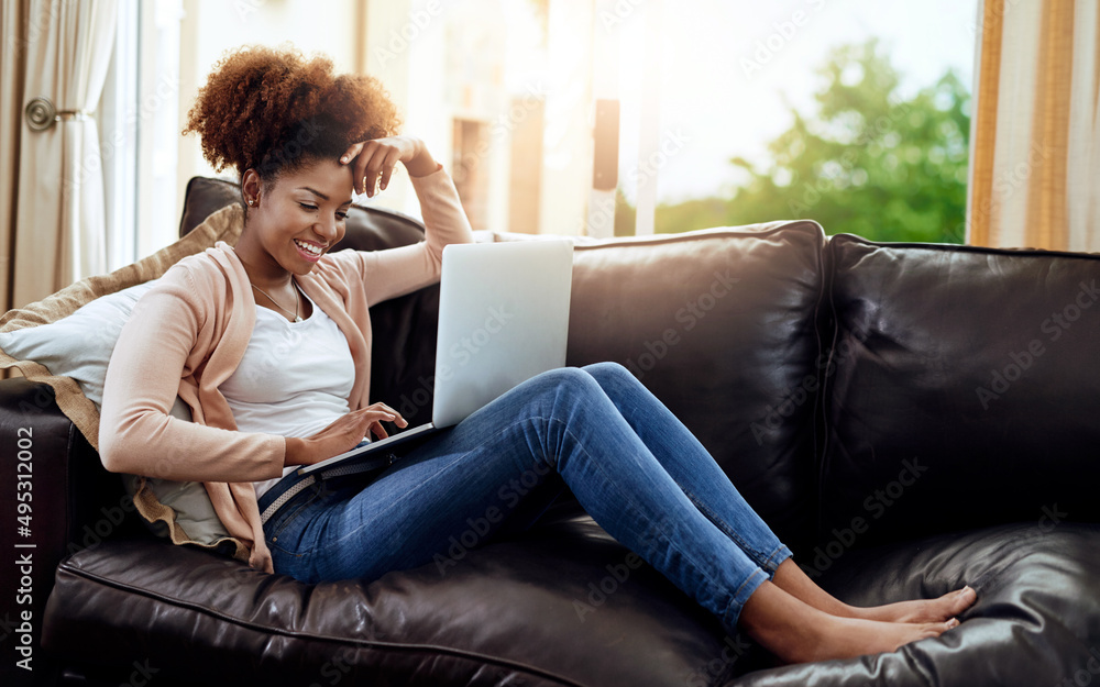 Having a solo movie date. Shot of a relaxed young woman using a laptop on the sofa at home.