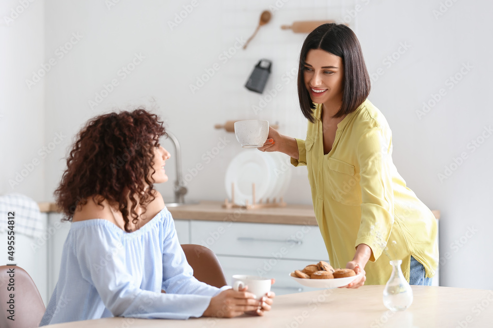 年轻女子在厨房里拿着杯子，把装有饼干的盘子送给她的妹妹