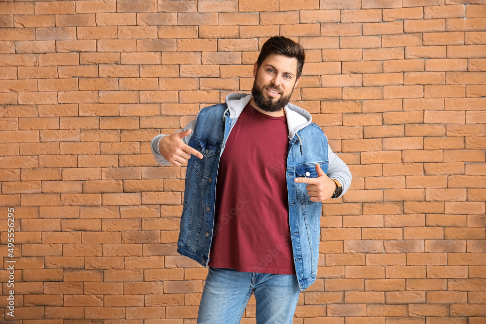 Handsome man pointing at red t-shirt on brick background