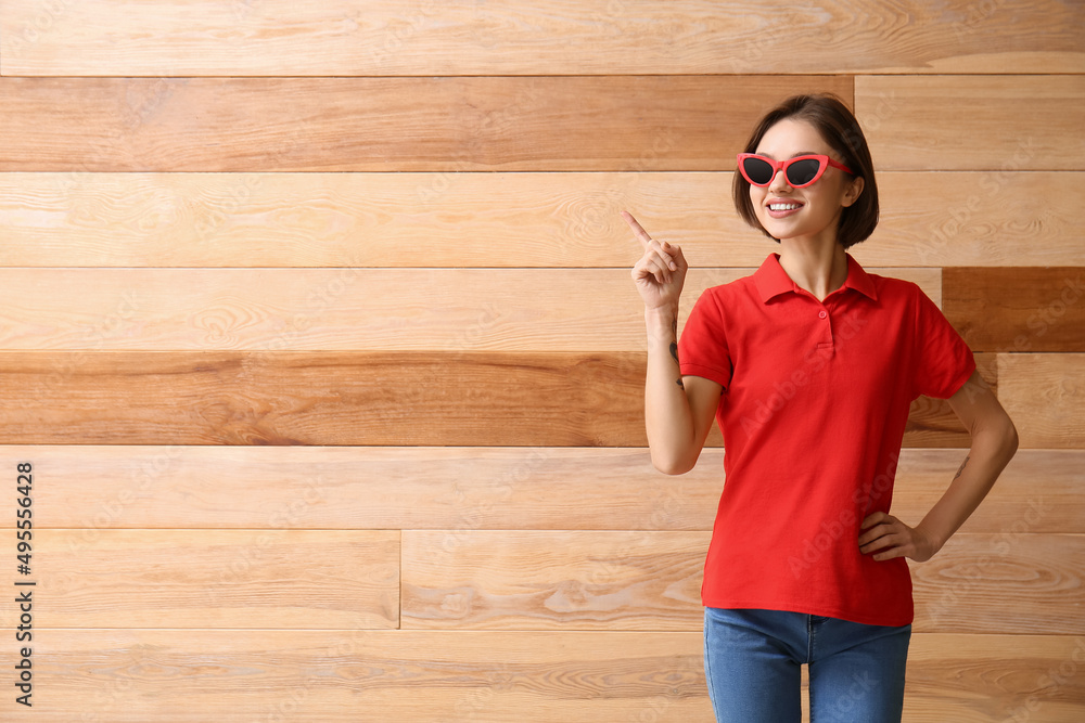 Beautiful young woman in stylish polo shirt pointing at something on wooden background