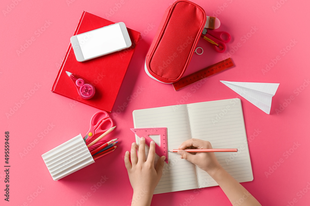 Childs hands with stationery and mobile phone on pink background