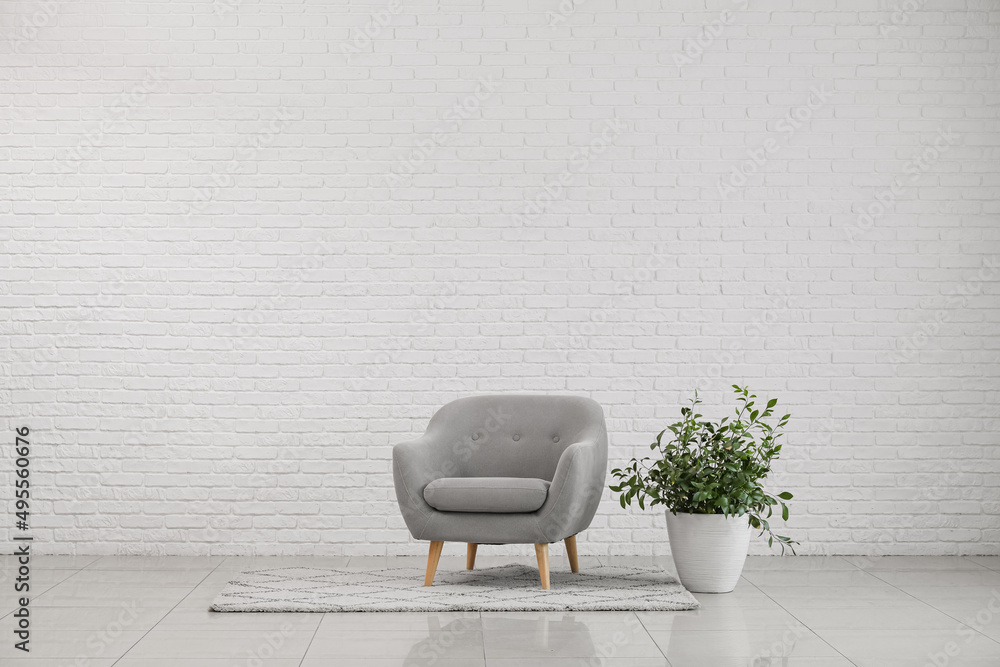 Modern armchair with houseplant near white brick wall