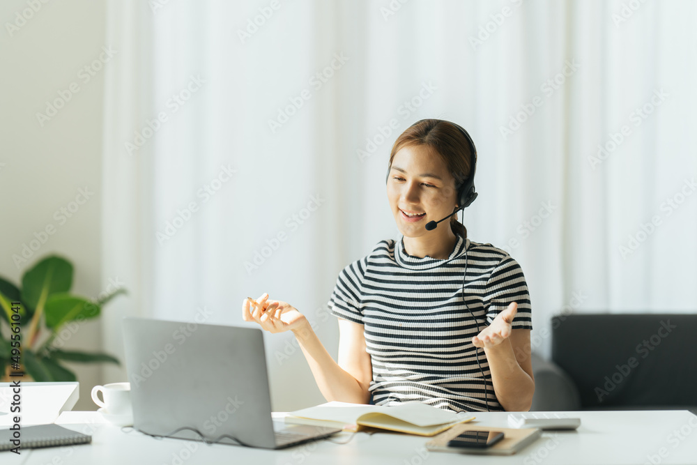 Happy young businesswoman wearing earphones, enjoying studying online, writing notes. Smiling creati