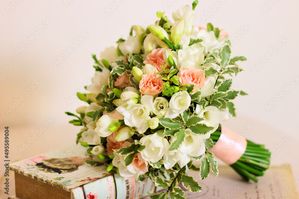 Bouquet of freesia flower, roses and light leaves and book on light pink background. Handle of bouqu