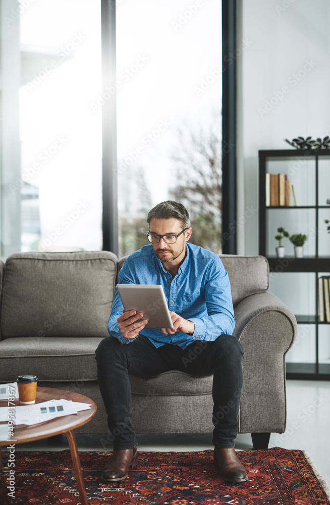 The tool of his trade. Shot of a businessman using his digital tablet while sitting on a sofa in the