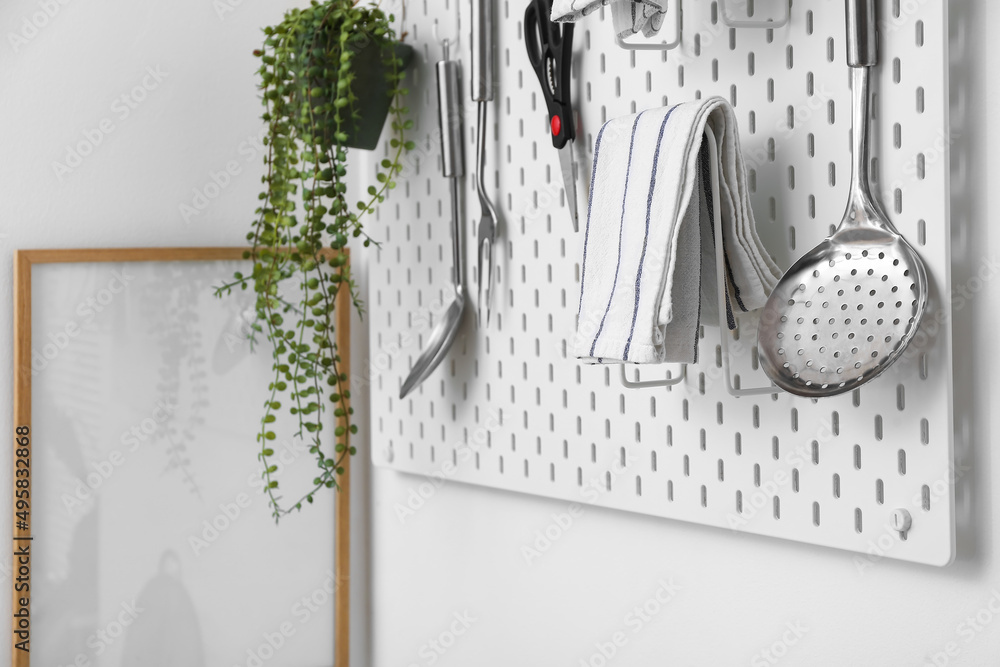 Pegboard with modern kitchenware and houseplant on white wall