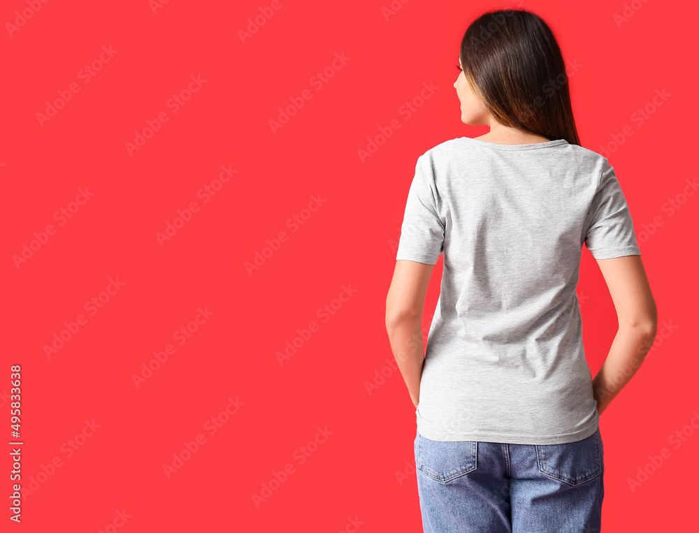 Young woman in blank t-shirt on color background, back view