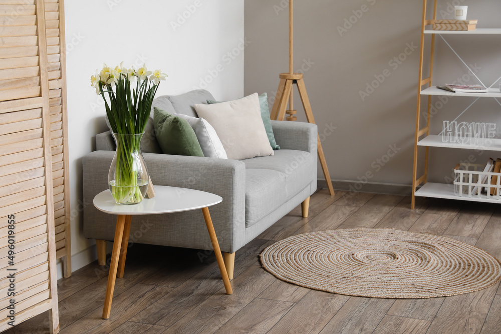 Interior of light living room with sofa, table and daffodils in vase