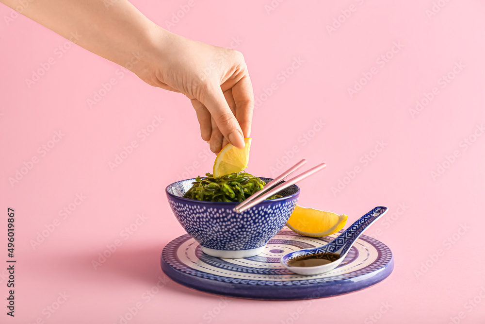 Woman putting lemon slice in healthy seaweed salad on pink background