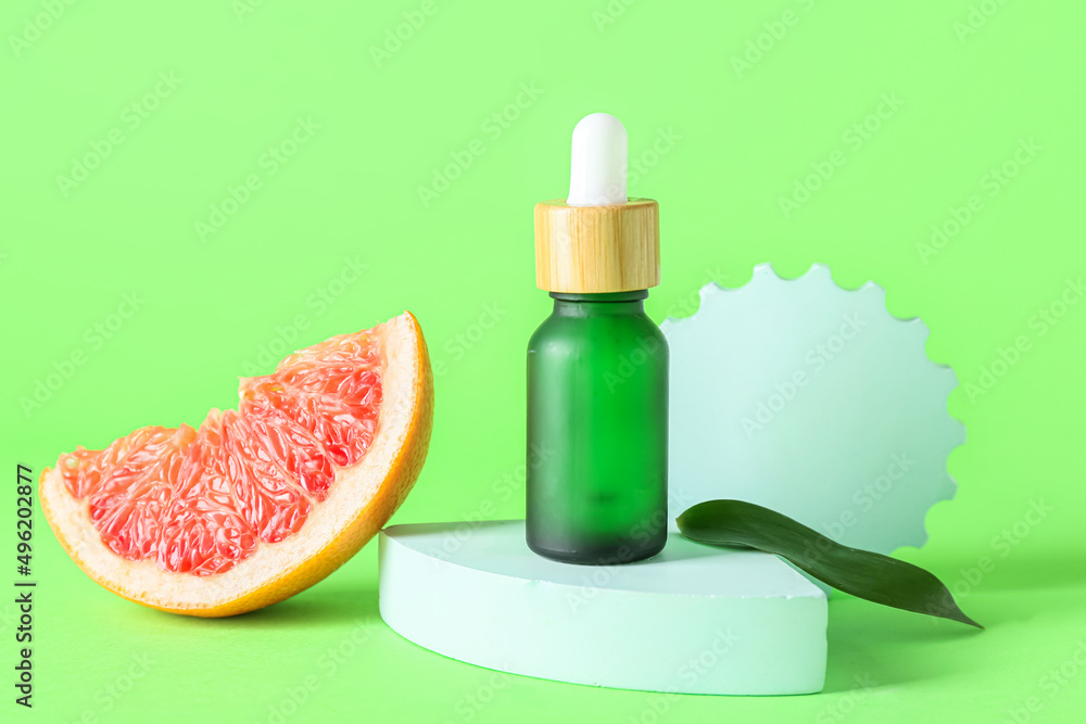 Composition with bottle of essential oil and grapefruit slice on green background