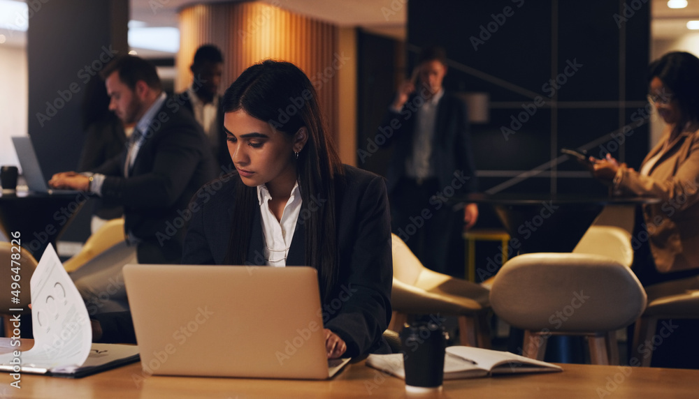 Staying late with the rest of her team. Shot of a young businesswoman going through paperwork while 