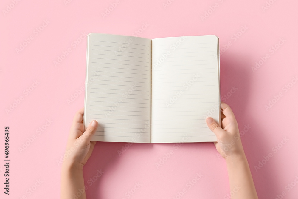 Childs hands with blank open notebook on pink background