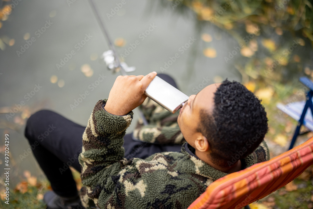 西班牙裔男子在湖上钓鱼时从金属瓶里喝了一些酒。nat休闲的概念