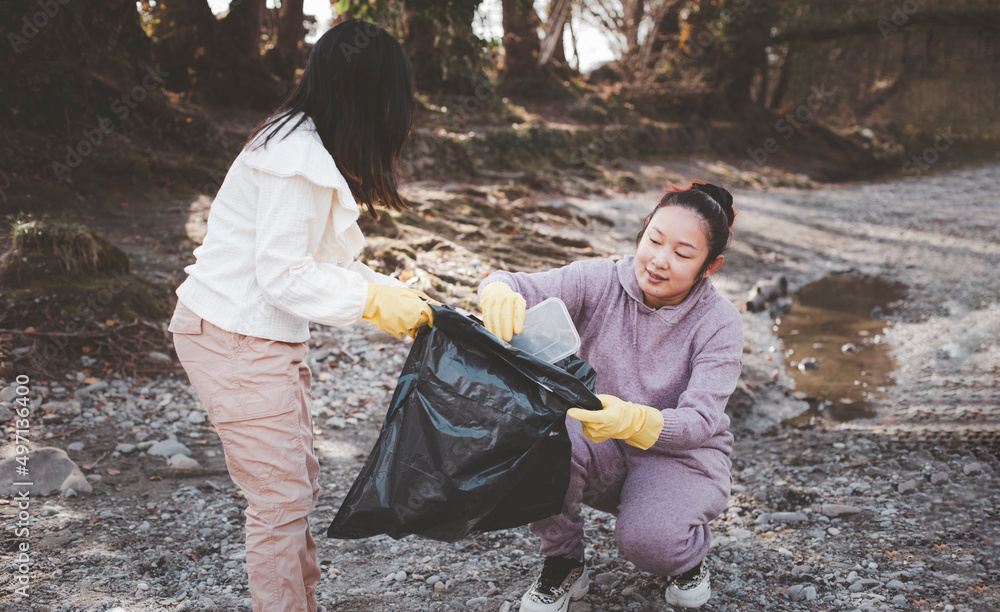 地球日概念，妇女和女儿用垃圾袋捡垃圾，在大自然中进行清理以回收