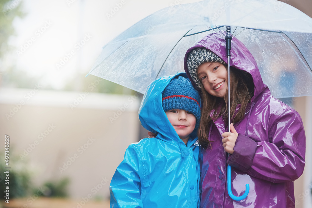 雨从未阻止我们玩得开心。两个兄弟姐妹站在外面的雨伞下的肖像