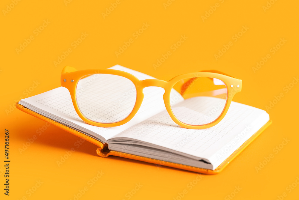 Stylish eyeglasses and open notebook on color background