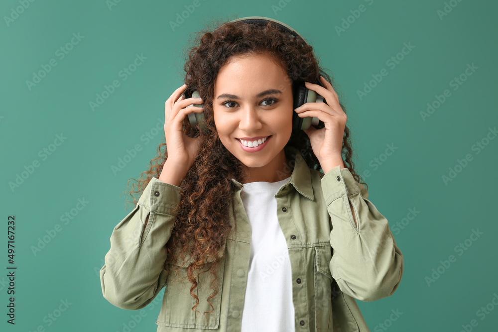 Young African-American woman in headphones listening to music on green background