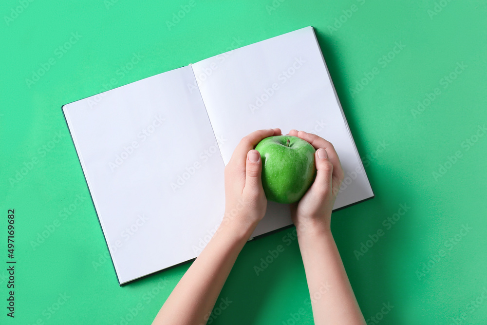 Childs hands with apple and blank book on green background