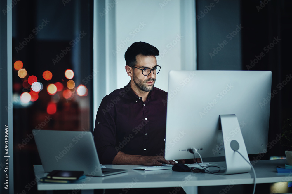 Staying late to get it done. Shot of a young businessman using a computer at his desk during a late 