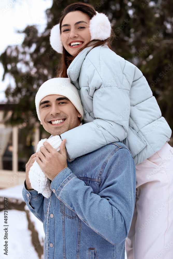 Happy young man carrying his girlfriend on piggyback on snowy winter day