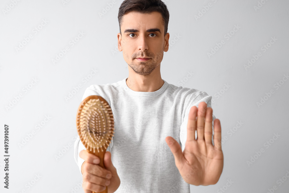 Handsome man with comb and fallen down hair showing stop gesture on light background