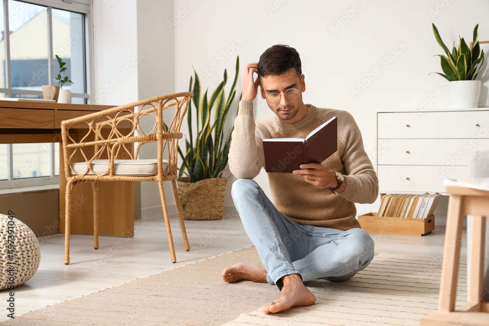 Young barefooted man reading book at home