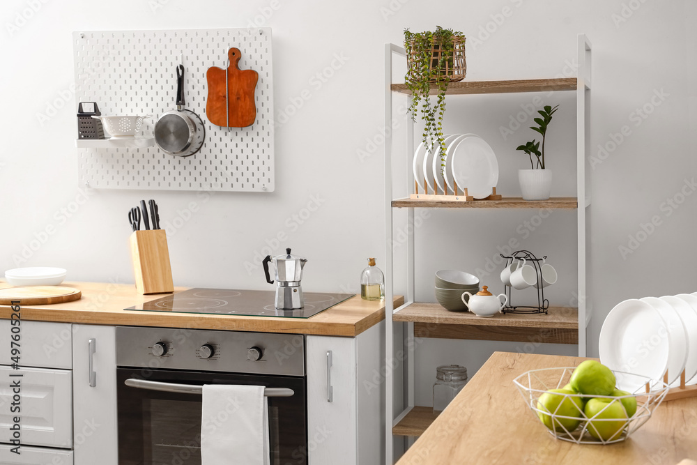 Modern shelving unit, pegboard and kitchen counter with stove near light wall