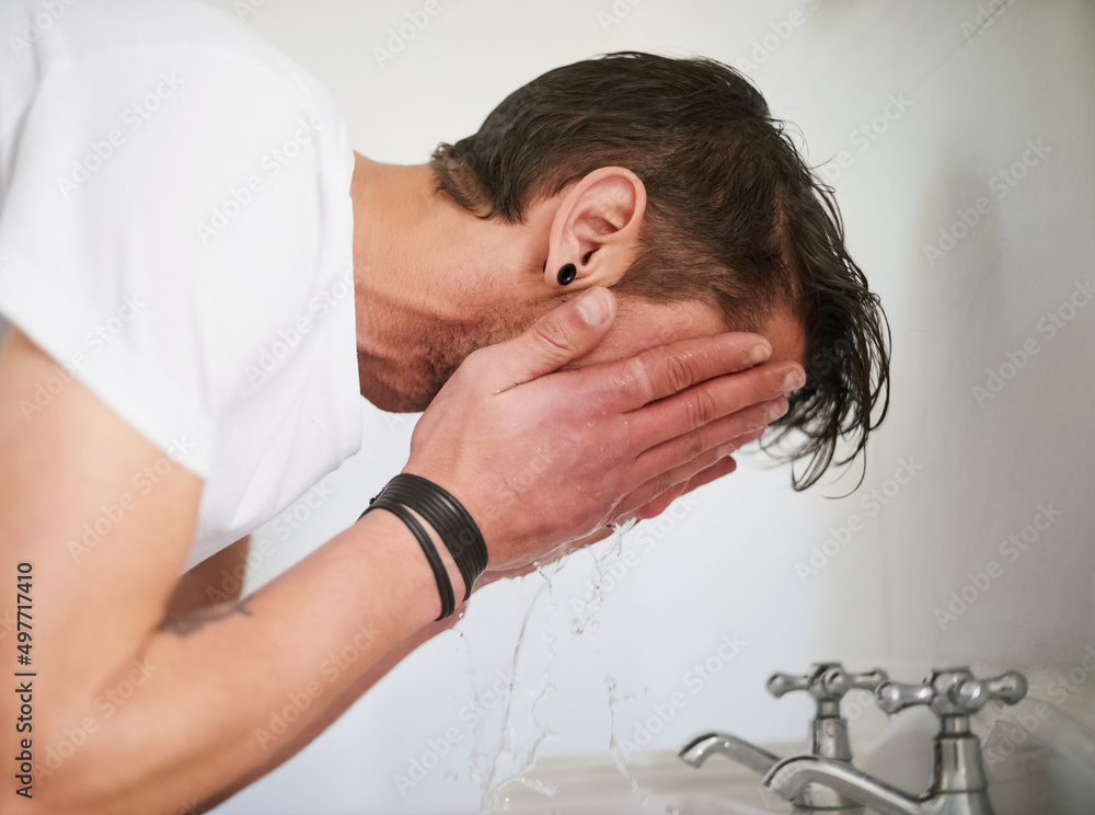 Freshening up in the morning. Shot of a young man washing his face in a bathroom sink.