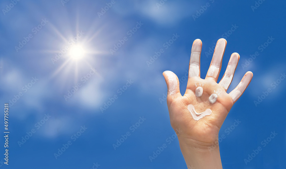 Positive symbol drawing by sunscreen (sun cream, suntan lotion) on open hand on blue sky background.