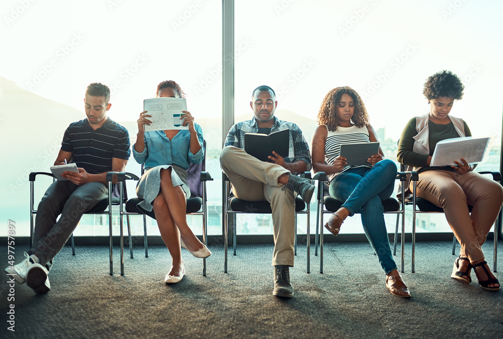 Shot of a group of young focussed work colleagues seated on chairs next to each other in a row while