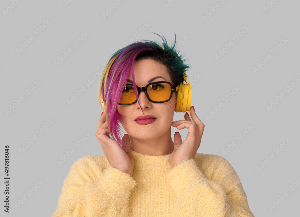 Beautiful woman with unusual hair listening to music on grey background