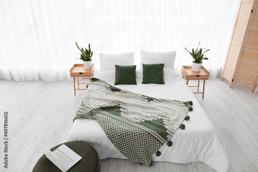 Comfortable bed, nightstands and houseplants in room