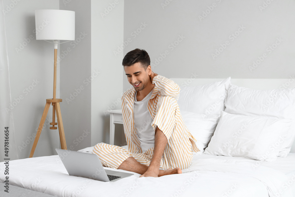 Young barefooted man using laptop in bedroom