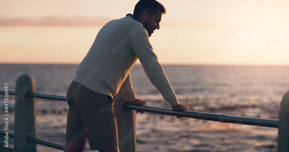 Ending off a long day at the beach. Rearview shot of a man watching the sun set at the beach.