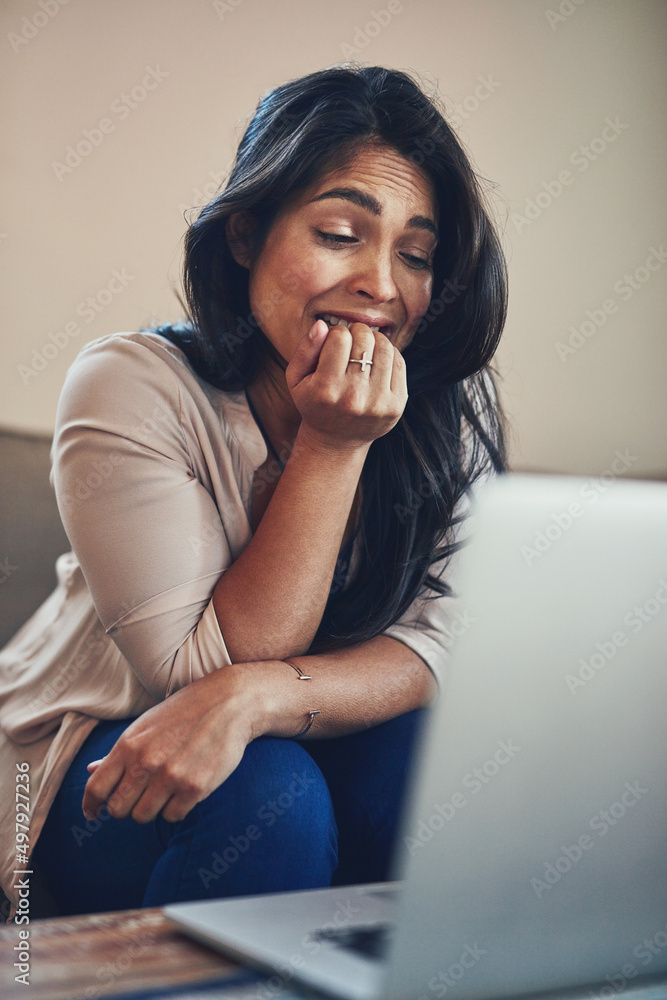 Her nerves are shot. Shot of a young woman biting her nails while working on a laptop at home.