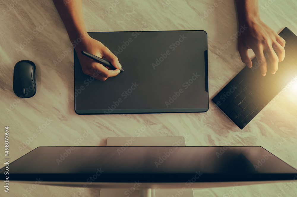 Top view of a designer using a graphics tablet at work on a desktop computer.