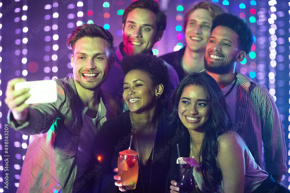 Everybody say cheese. Shot of a happy group of friends taking a selfie with a smartphone in a nightc